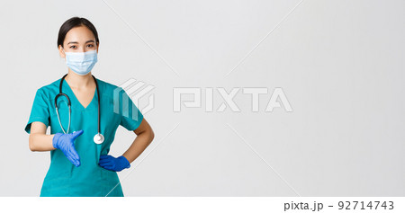 Covid-19, coronavirus disease, healthcare workers concept. Confident young asian female doctor, physician in scrubs and medical mask, gloves, extend hand for handshake, greeting patient Covid-19, coronavirus disease, healthcare workers concept. Confident young asian female doctor, physician in scrubs and medical mask, gloves, extend hand for handshake, greeting patient 92714743