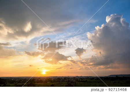 Dramatic sunset landscape with puffy clouds lit by orange setting sun and blue sky. Dramatic sunset landscape with puffy clouds lit by orange setting sun and blue sky. 92715408