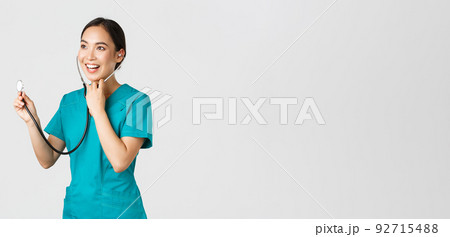 Covid-19, healthcare workers and preventing virus concept. Smiling friendly-looking asian female doctor listening to patient lungs during daily checkup, using stethoscope, white background 92715488
