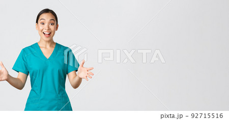 Covid-19, healthcare workers, pandemic concept. Happy and surprised asian nurse in scrubs raising hands excited and smiling. Doctor congratulate with great news, applause, white background 92715516