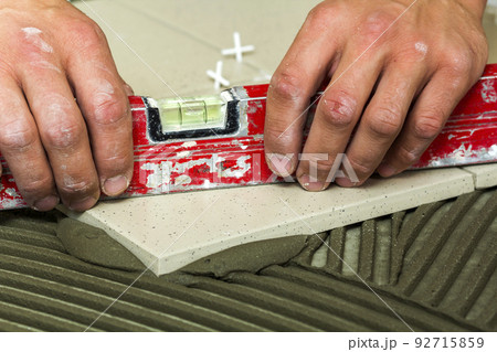 Ceramic tiles and tools for tiler. Worker hand installing floor tiles. Home improvement, renovation - ceramic tile floor adhesive, mortar, level. Ceramic tiles and tools for tiler. Worker hand installing floor tiles. Home improvement, renovation - ceramic tile floor adhesive, mortar, level. 92715859