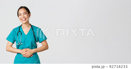 Covid-19, healthcare workers, pandemic concept. Happy pretty asian female doctor, physician in scrubs having fun, laughing and touching belly while joking around with hospital staff Covid-19, healthcare workers, pandemic concept. Happy pretty asian female doctor, physician in scrubs having fun, laughing and touching belly while joking around with hospital staff 92716233