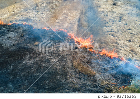 Aerial view of grassland field burning with red fire during dry season. Natural disaster and climate change concept Aerial view of grassland field burning with red fire during dry season. Natural disaster and climate change concept 92716265