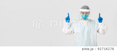 Covid-19, coronavirus disease, healthcare workers concept. Serious-looking young asian female doctor, tech lab employee in respirator and personal protective equipment, white background 92716276