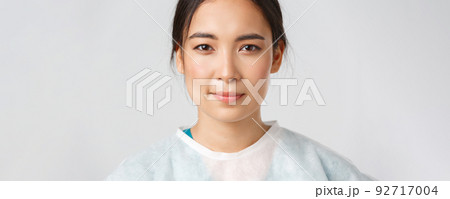 Covid-19, coronavirus disease, healthcare workers concept. Close-up of hopeful exhausted, smiling asian female doctor take-off personal protective equipment, have skin marks from respirator 92717004