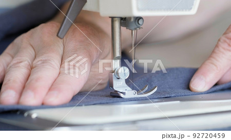 Hands of seamstress sewing with a professional machine, embroiders sews on grey fabric. Hands of seamstress sewing with a professional machine, embroiders sews on grey fabric. 92720459