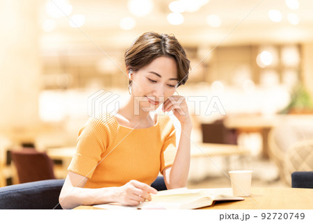 カフェで音楽を聴きながら読書するミドルの女性 92720749