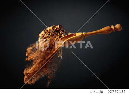Cinnamon powder is poured out of the wooden spoon. 92722185