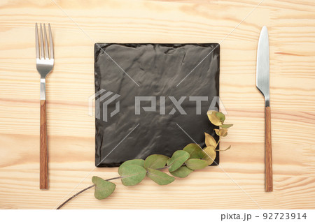 Mockup Blank board and cutlery. Knife and fork with black stone board for menu or recipe text and gold eucalyptus branch. Flat lay with mockup food menu on wooden table Mockup Blank board and cutlery. Knife and fork with black stone board for menu or recipe text and gold eucalyptus branch. Flat lay with mockup food menu on wooden table 92723914