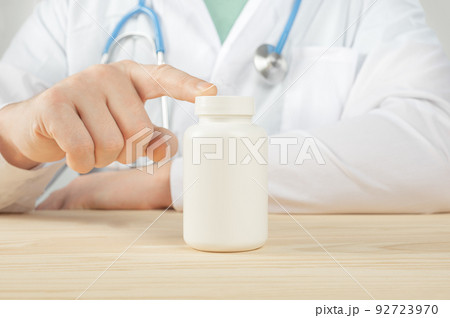 doctor holding white bottle of tablets or pills with a blank white label for treatment of an illness or injury. Doctor's appointment blank pills bottle. doctor holding white bottle of tablets or pills with a blank white label for treatment of an illness or injury. Doctor's appointment blank pills bottle. 92723970
