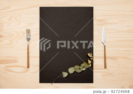 Mockup Blank card a4, a3 and cutlery on rustic wooden background. Knife and fork with black paper for menu or recipe text and gold eucalyptus branch. Flat lay with mockup food menu on wooden table 92724008