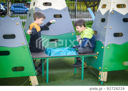 Two Boys playing with modern spin top outdoors. Entertainment game for children. Top, triggered by a trigger. Kids having a tournament on arena or battle field Two Boys playing with modern spin top outdoors. Entertainment game for children. Top, triggered by a trigger. Kids having a tournament on arena or battle field 92728226