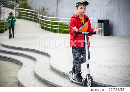 Happy family lifestyle and holiday concept. little boy and his sibling brother riding scooters, walking in city, street. Having fun Happy family lifestyle and holiday concept. little boy and his sibling brother riding scooters, walking in city, street. Having fun 92728524