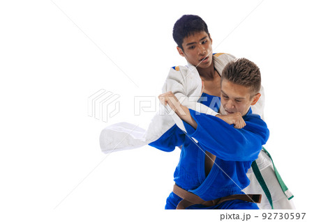 Dynamic portrait of two young men, professional judo athletes training, fighting isolated over white background 92730597