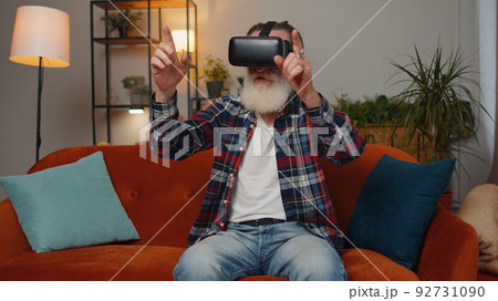 Senior man using virtual reality futuristic technology headset play simulation 3D video game at home Senior man using virtual reality futuristic technology headset play simulation 3D video game at home 92731090