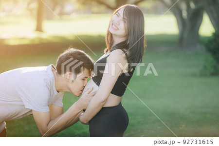 Portrait of lovely couple outdoors. Women pregnancy with her husband kiss on her belly. 92731615
