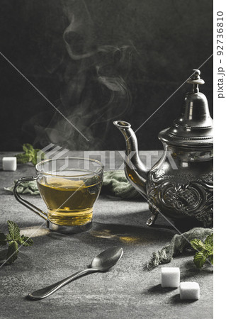Traditional Moroccan teapot with a steaming cup of tea in a smoky black atmosphere. Vertical format. 92736810