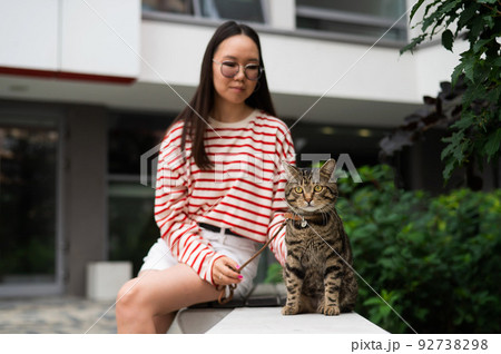 Young woman and tabby cat sitting on a bench outdoors. 92738298