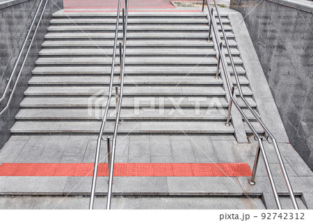 gray granite staircase with steps and stainless steel iron railings descent to the underground passage, entrance to the subway with tactile red tiles and a ramp for the disabled, top view, nobody. gray granite staircase with steps and stainless steel iron railings descent to the underground passage, entrance to the subway with tactile red tiles and a ramp for the disabled, top view, nobody. 92742312