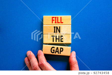 Fill in the gap symbol. Concept words Fill in the gap on wooden blocks on a beautiful blue table blue background. Businessman hand. Business, motivational and fill in the gap concept. 92743458