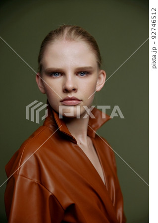 Stylish serious young blonde girl with blue eyes with evening makeup in a leather dress looks at the camera posing isolated. Studio portrait on a green background. Fashion offer Stylish serious young blonde girl with blue eyes with evening makeup in a leather dress looks at the camera posing isolated. Studio portrait on a green background. Fashion offer 92746512