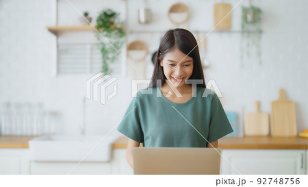Smiling asian young woman working on laptop at home office Smiling asian young woman working on laptop at home office 92748756