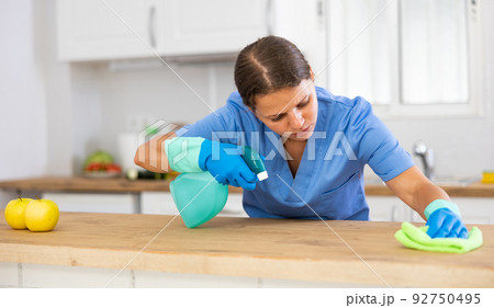 Young woman professional cleaner cleaning desk with detergents in kitchen 92750495