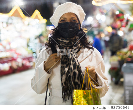 Hispanic woman in protective mask looking for festive decorations on city Christmas fair 92750645