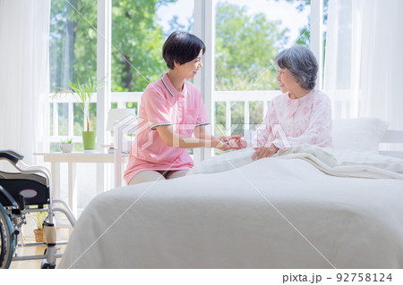 介護　ベットから起きあがるシニアを介助する介護士 92758124