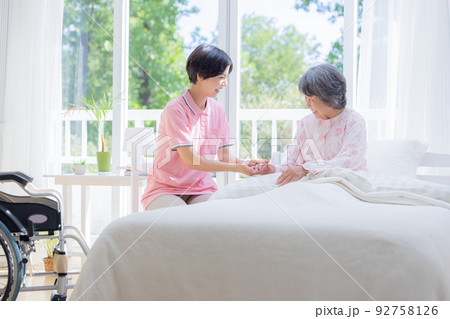 介護　ベットから起きあがるシニアを介助する介護士 92758126