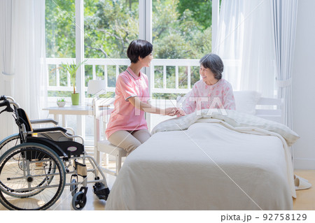 介護　ベットから起きあがるシニアを介助する介護士 92758129