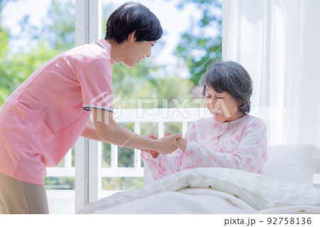介護 ベットから起きあがるシニアを介助する介護士 介護 ベットから起きあがるシニアを介助する介護士 92758136