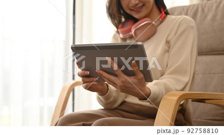 Cropped view smiling young woman watching videos, surfing internet on digital tablet in living room Cropped view smiling young woman watching videos, surfing internet on digital tablet in living room 92758810