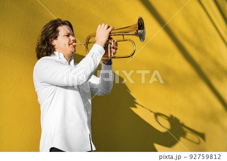 Young caucasian long-haired man in shirt playing trumpet outside on festival Young caucasian long-haired man in shirt playing trumpet outside on festival 92759812