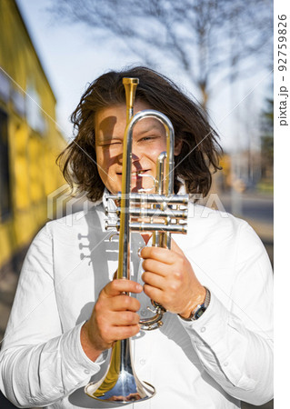 Young caucasian male cheerful jazzman looking through trumpet on sunny street Young caucasian male cheerful jazzman looking through trumpet on sunny street 92759826