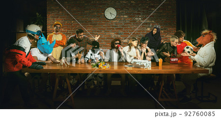 Group of people sitting at the long wooden table in different costumes, indoors Group of people sitting at the long wooden table in different costumes, indoors 92760085