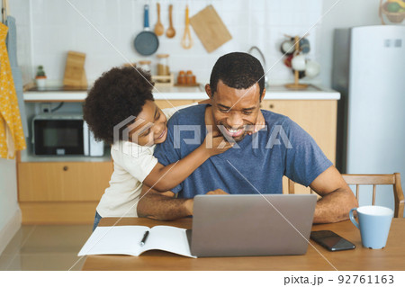 African American father working from home on laptop while his Cheerful son distracts 92761163