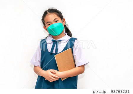 Portrait student Asian child girl in uniform, holding a book, wearing face mask for protection in era of covid virus, isolated student child girl on white background, concept for back to school. Portrait student Asian child girl in uniform, holding a book, wearing face mask for protection in era of covid virus, isolated student child girl on white background, concept for back to school. 92763281