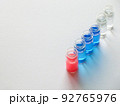 白い画用紙の上に斜めに並べた青色と赤色と透明な液体が入った6個のガラス瓶 92765976