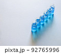白い画用紙の上に斜めに並べた青色の液体が入った6個のガラス瓶 92765996