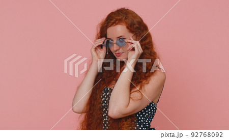 Seductive cheerful ginger stylish girl in dress wearing sunglasses, charming smile on pink wall Seductive cheerful ginger stylish girl in dress wearing sunglasses, charming smile on pink wall 92768092