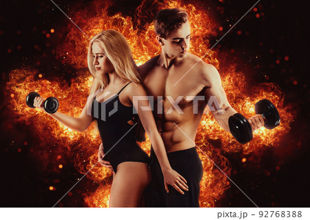 Muscular couple body in studio. Couple of fit bodybuilders, muscular man and beautiful sexy girl with dumbbells. Sport couple. Fire background Muscular couple body in studio. Couple of fit bodybuilders, muscular man and beautiful sexy girl with dumbbells. Sport couple. Fire background 92768388