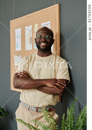 Portrait of African young businessman in eyeglasses standing with arms crossed at office and smiling at camera 92768506