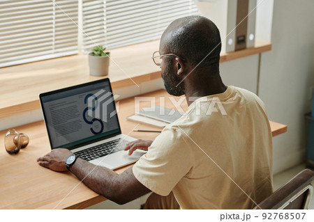 Rear view of African young businessman sitting at his workplace with laptop and typing document online 92768507