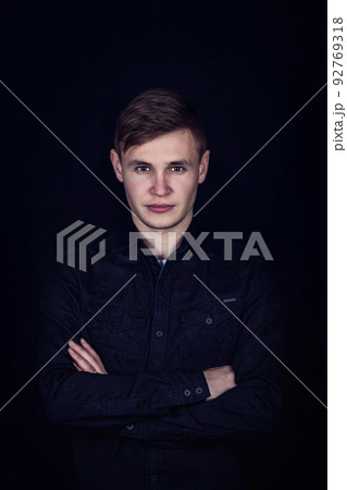 Young man hands crossed portrait isolated on dark background. Boy teenager looks confident to camera, keeps arms folded Young man hands crossed portrait isolated on dark background. Boy teenager looks confident to camera, keeps arms folded 92769318