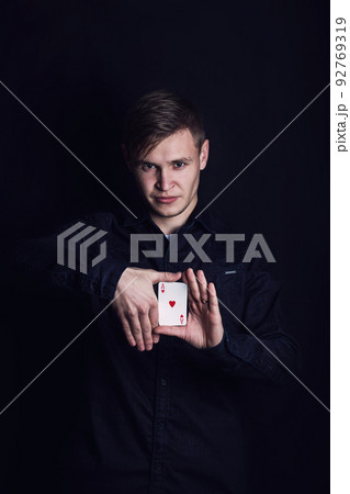 Confident young man showing tricks with playing cards like a magician, isolated on dark background. Gambling games winner, successful gambler showing illusions Confident young man showing tricks with playing cards like a magician, isolated on dark background. Gambling games winner, successful gambler showing illusions 92769319