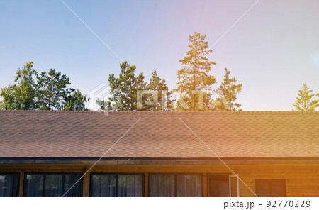 The roof of a wooden house is covered with flexible tiles in the rays of sunlight. Close-up 92770229
