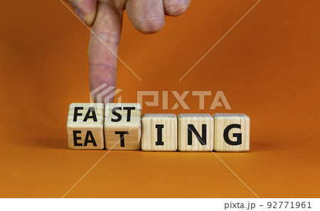 Fasting or eating symbol. Doctor turns wooden cubes and changes the word 'eating' to 'fasting'. Beautiful orange background, copy space. Healthy eating, medical and time to fasting concept. Fasting or eating symbol. Doctor turns wooden cubes and changes the word 'eating' to 'fasting'. Beautiful orange background, copy space. Healthy eating, medical and time to fasting concept. 92771961