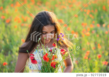 Beautiful girl in the poppy field. Holding beautiful flowers. summer time. Young girl smells flowers in the field 92772019