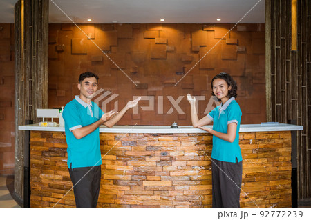 two employees wearing uniforms smiling with hand gestures presenting something 92772239